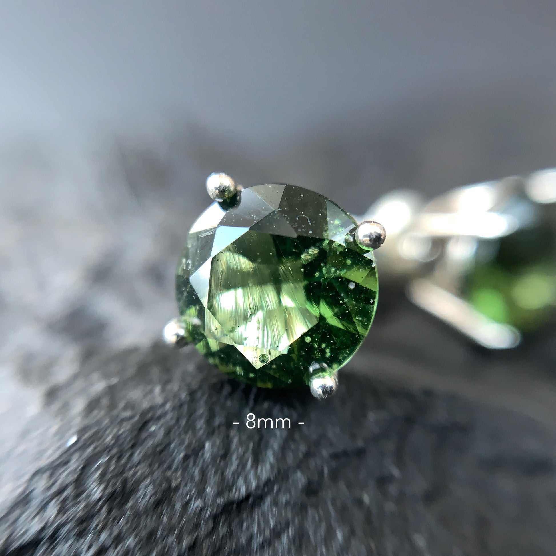 Close-up of a Moldavite earring 8 mm on a textured surface