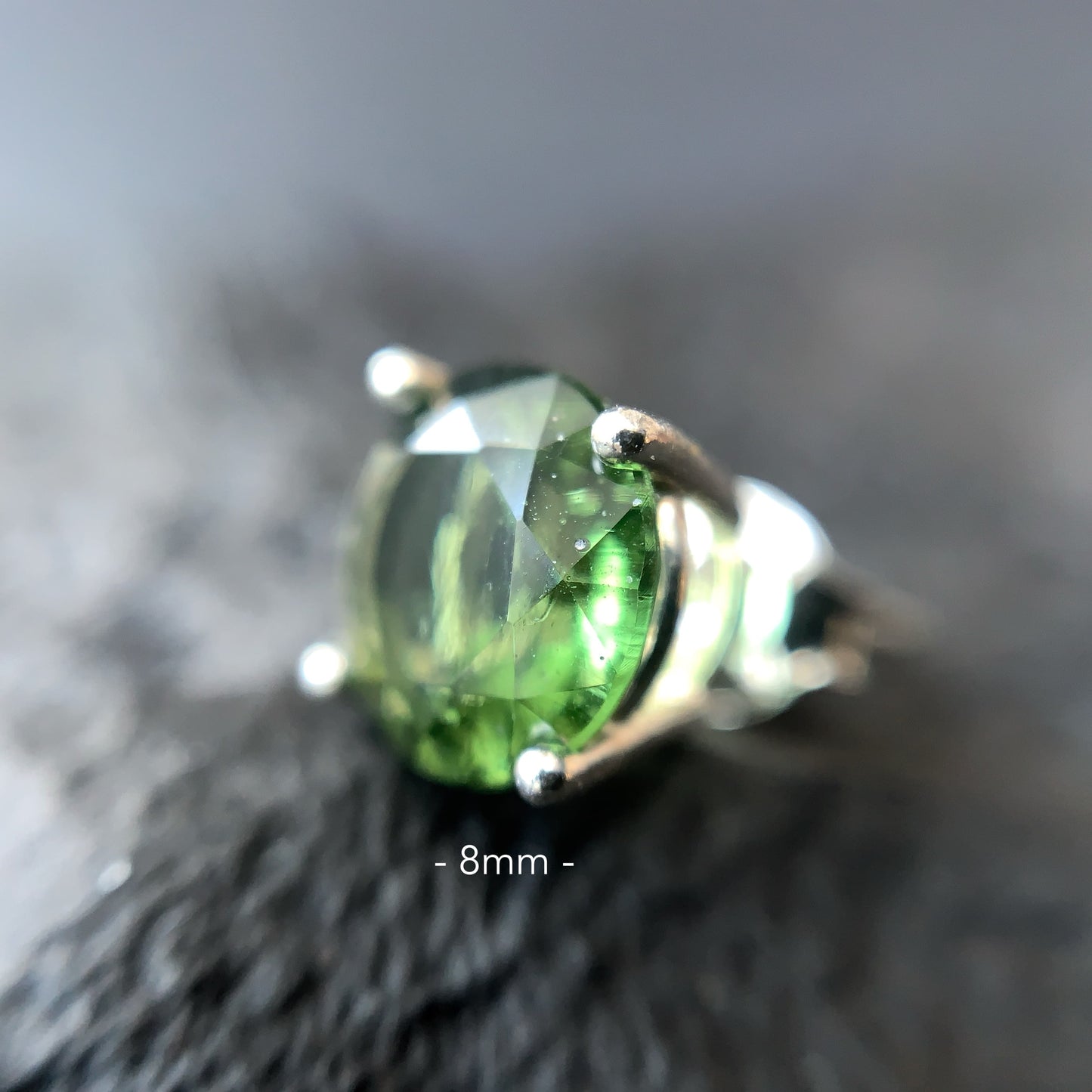 Close-up of a Moldavite earring 8 mm on a textured surface