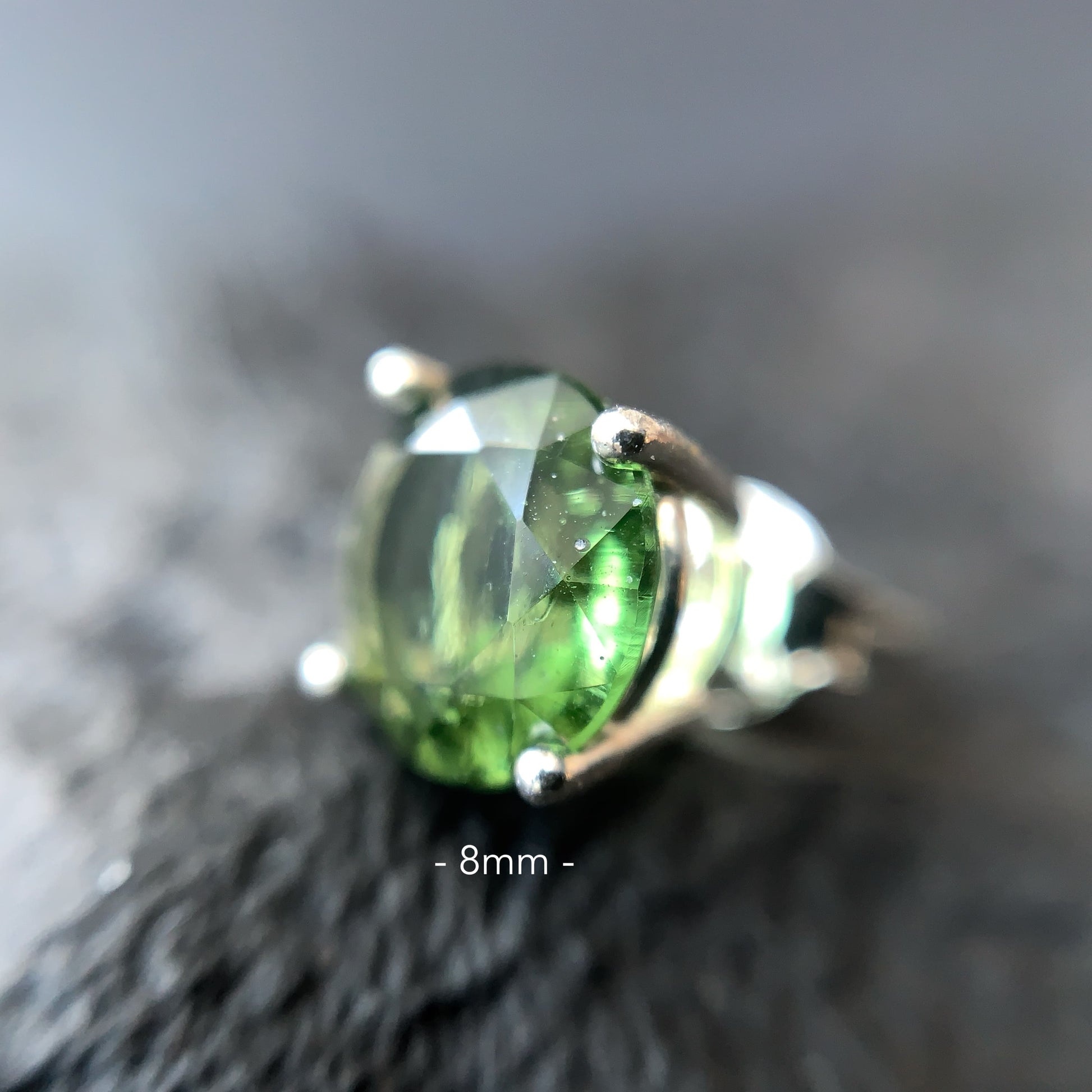 Close-up of a Moldavite earring 8 mm on a textured surface