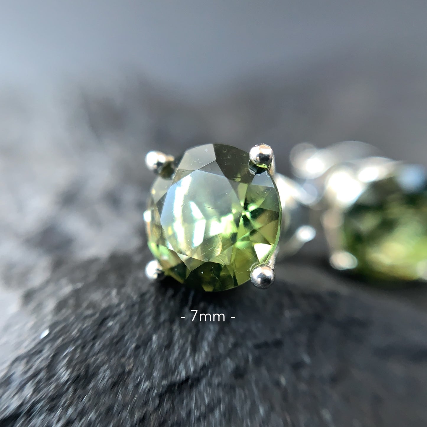 Close-up of a Moldavite earring 7 mm on a textured surface