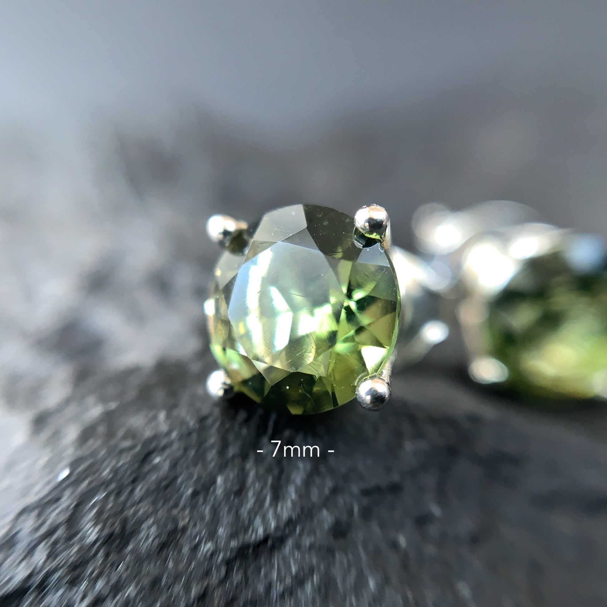 Close-up of a Moldavite earring 7 mm on a textured surface
