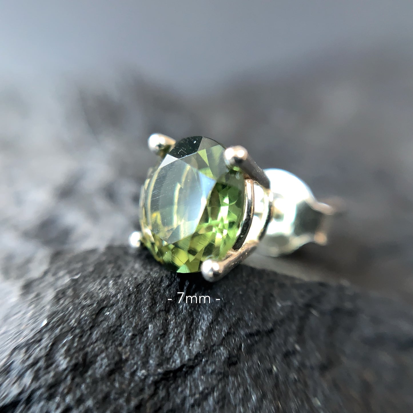 Close-up of a Moldavite earring 7 mm on a textured surface