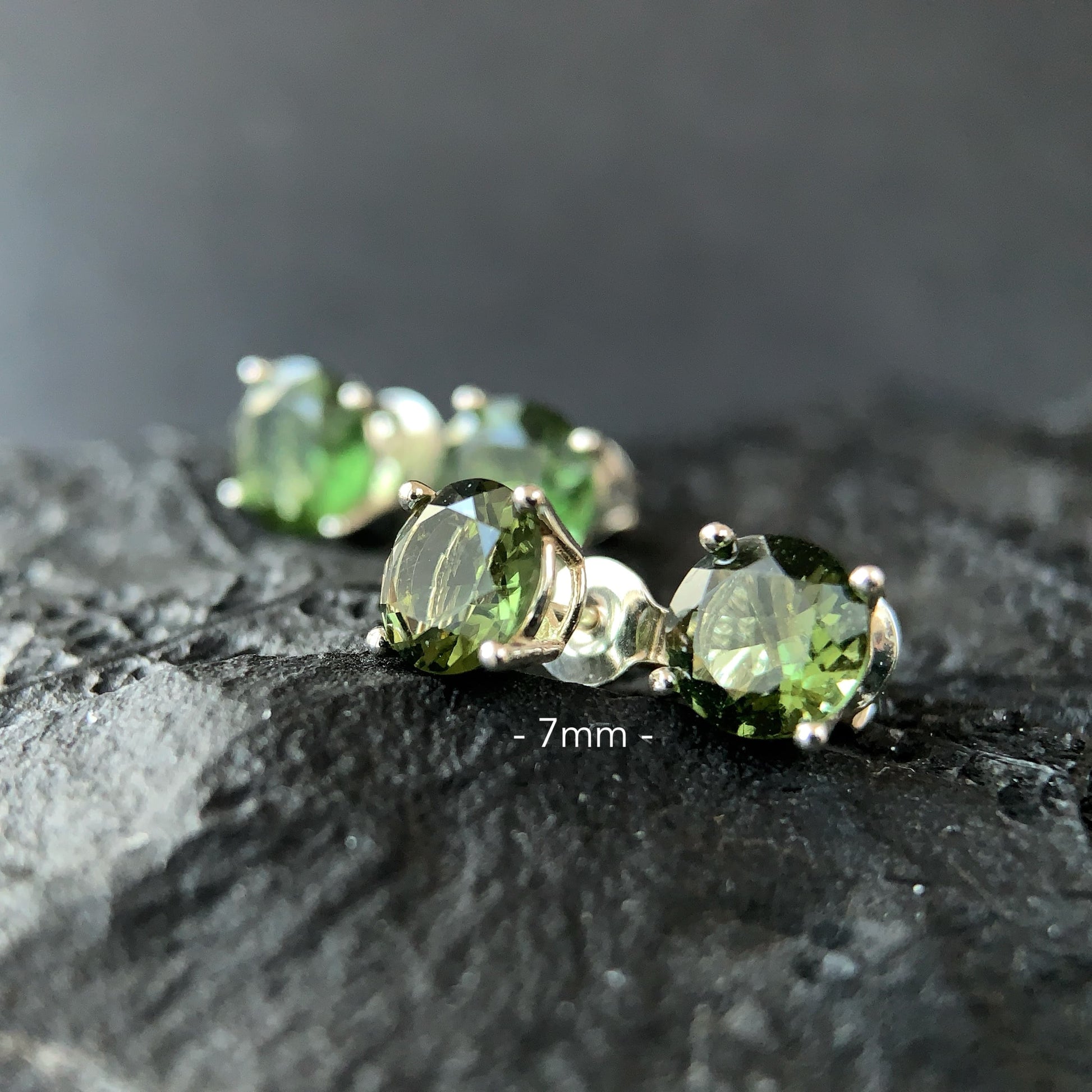 Moldavite stud earrings on a dark textured surface in 7 mm setting