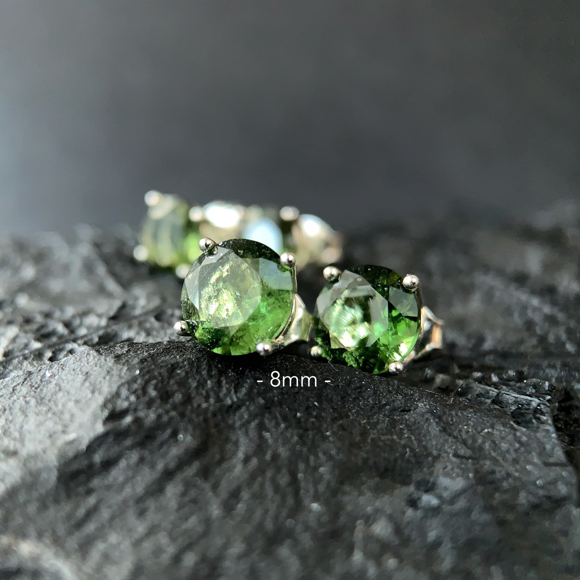 Moldavite stud earrings on a dark textured surface in 8mm setting