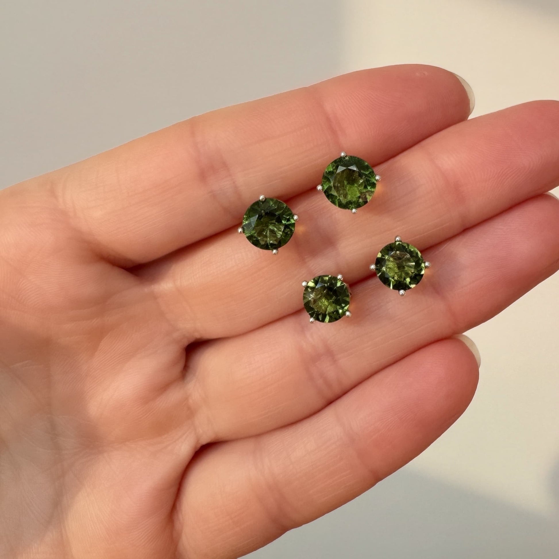 Moldavite stud earrings held in a hand against a neutral background showing size of each earring