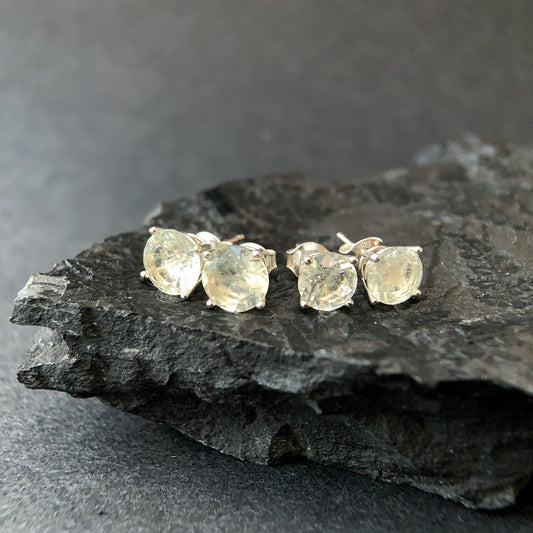 Libyan desert glass stud earrings on a dark stone surface