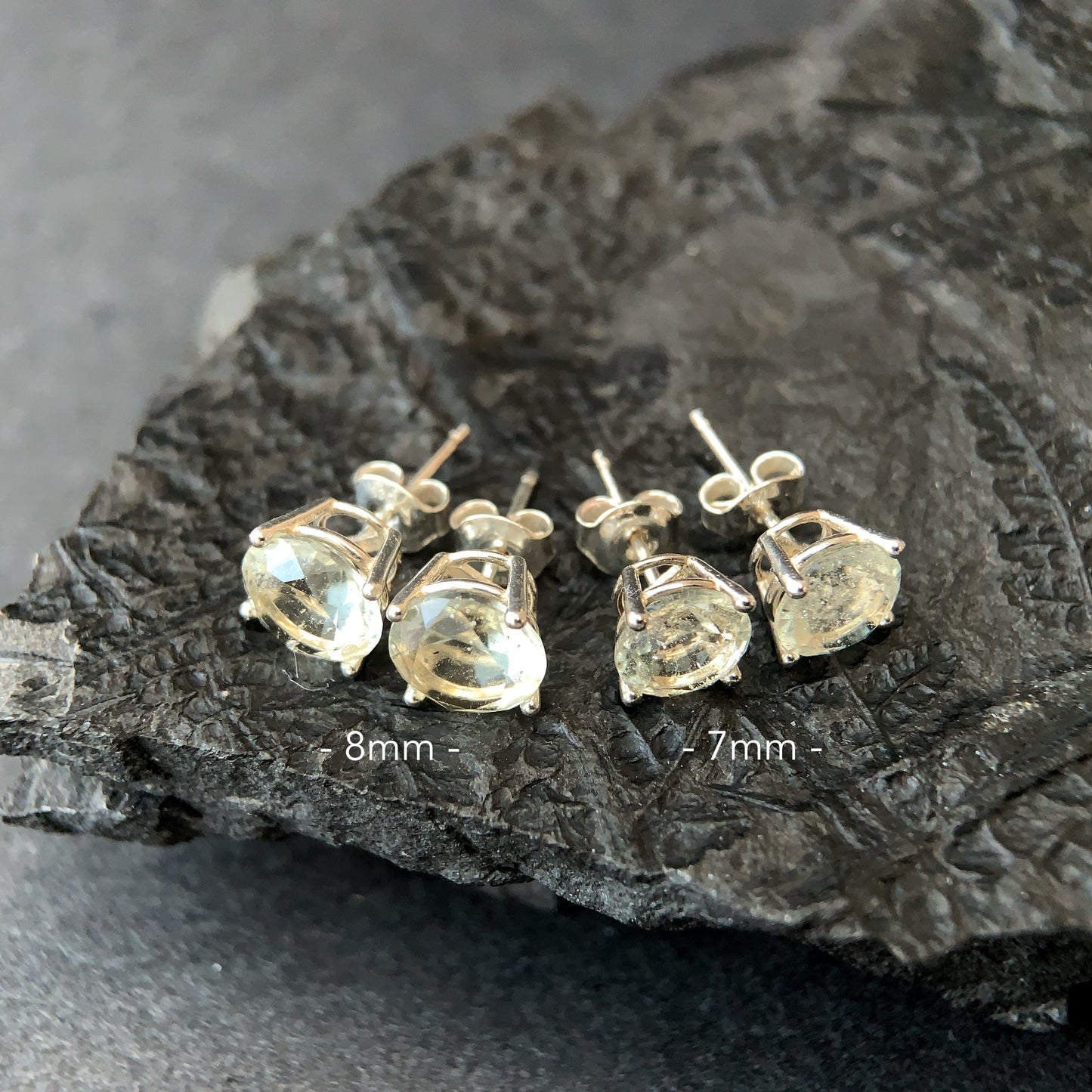 Two pairs of silver stud earrings with Libyan desert glass on a dark stone surface.