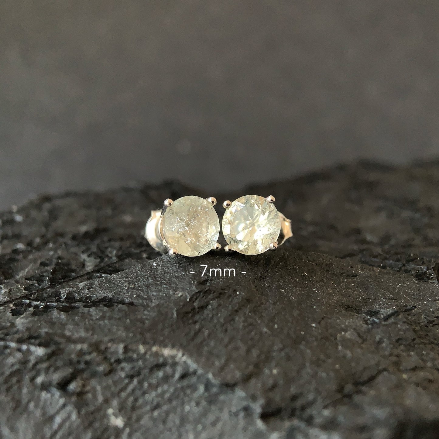 Pair of round earrings on a dark textured surface with '7mm' label.