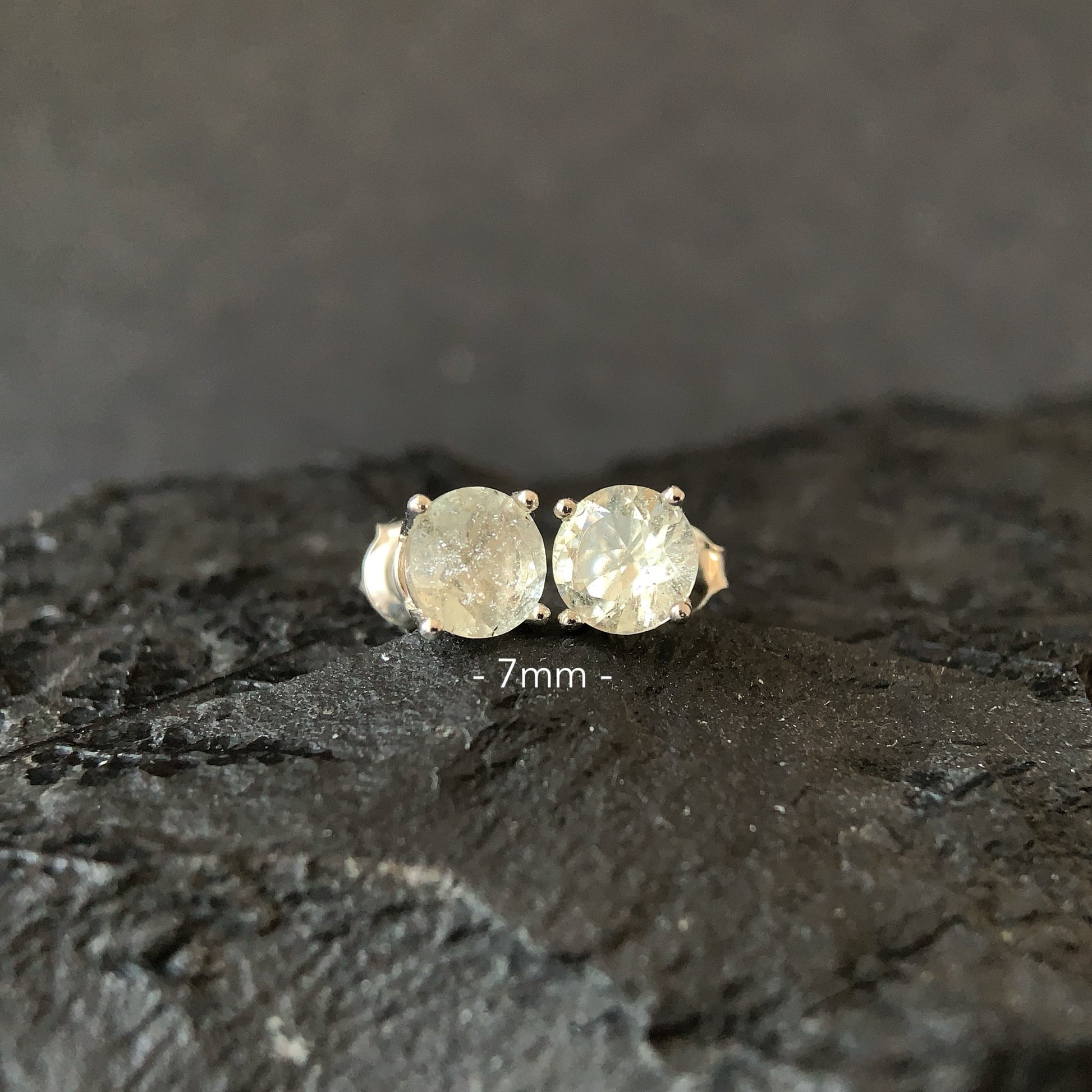 Pair of round earrings on a dark textured surface with '7mm' label.