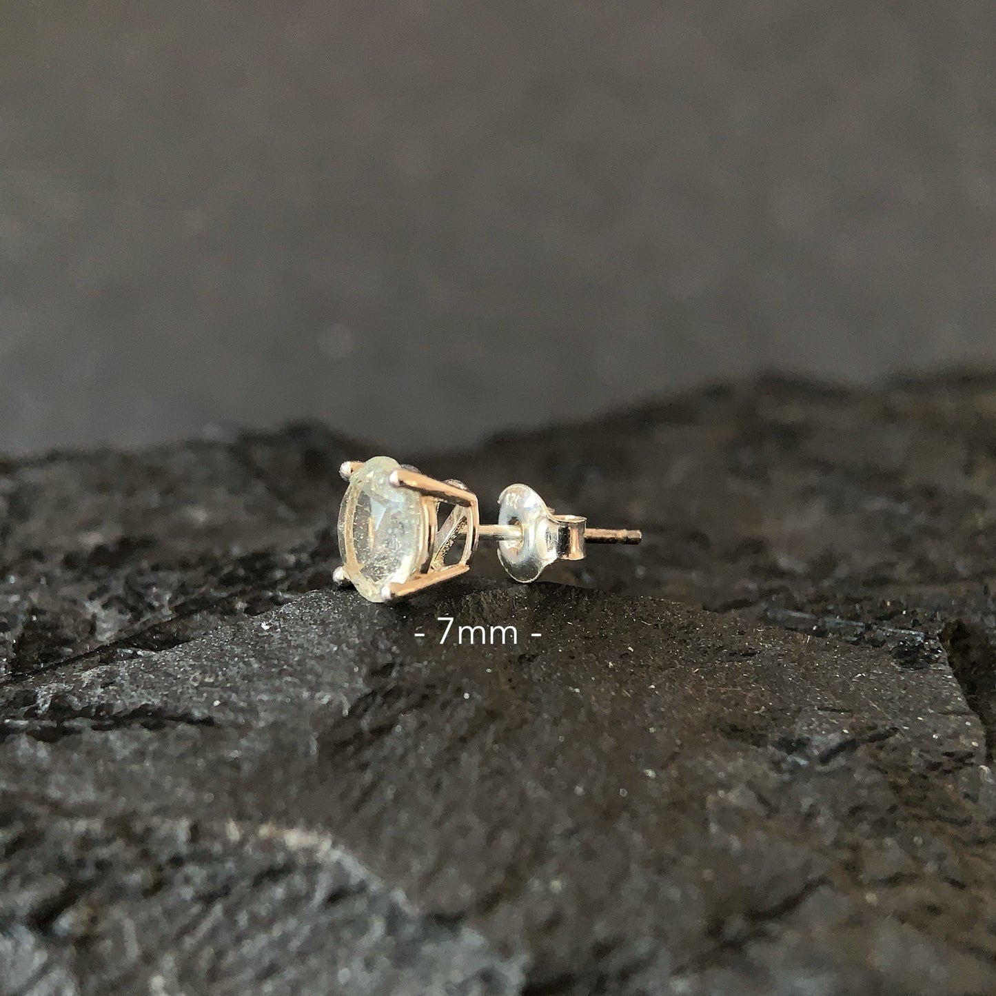 Libyan desert glass 7mm stud earring on a dark surface