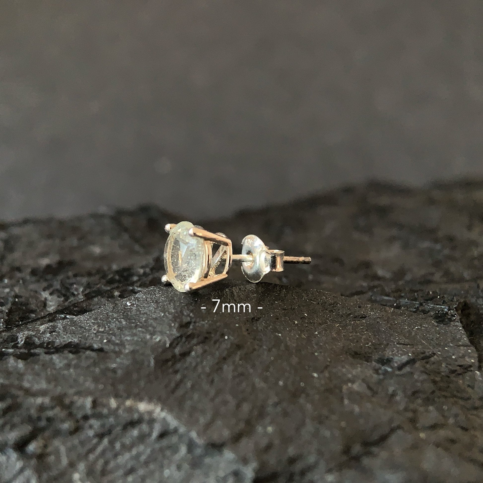 Libyan desert glass 7mm stud earring on a dark surface