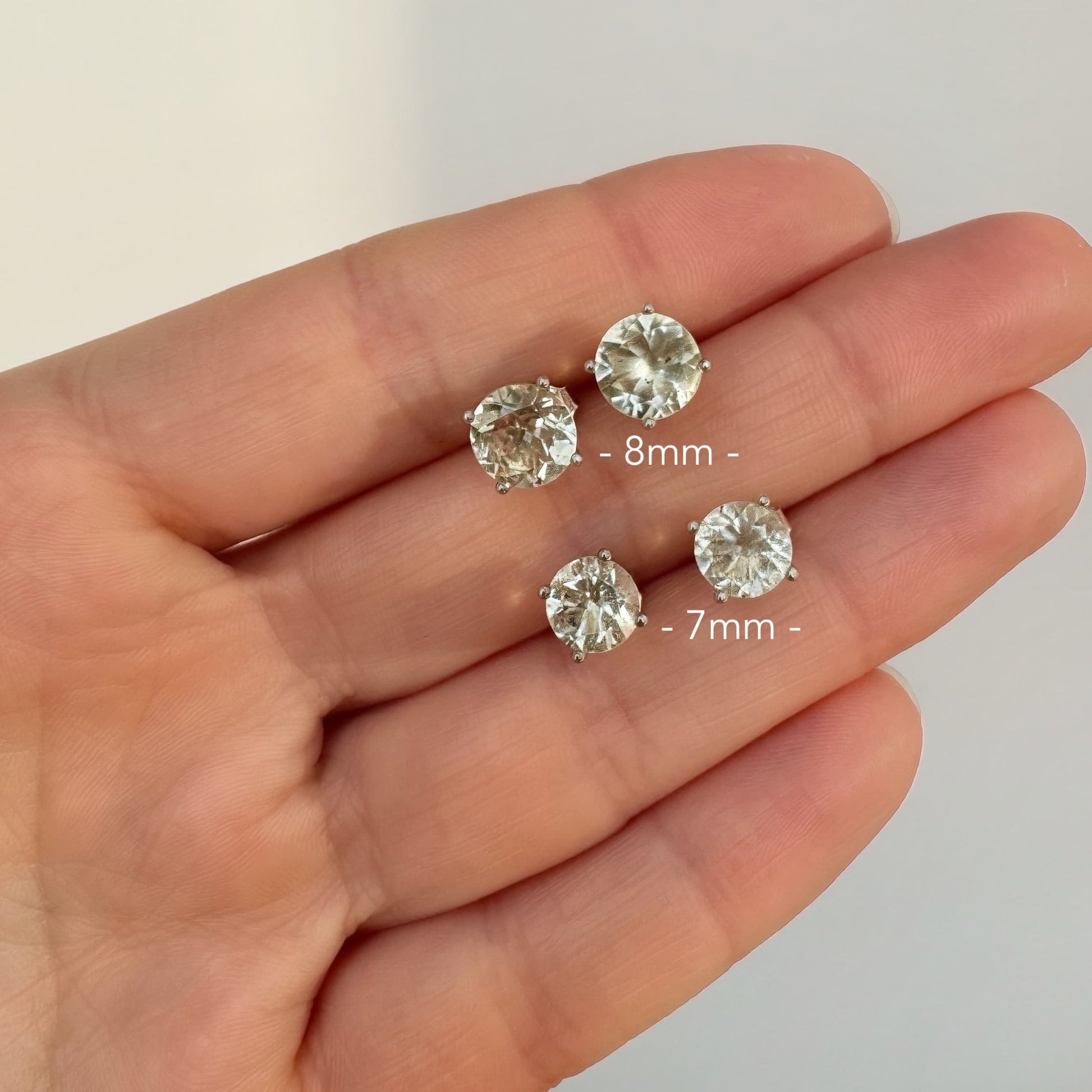 Libyan desert glass stud earrings on a hand with size labels.