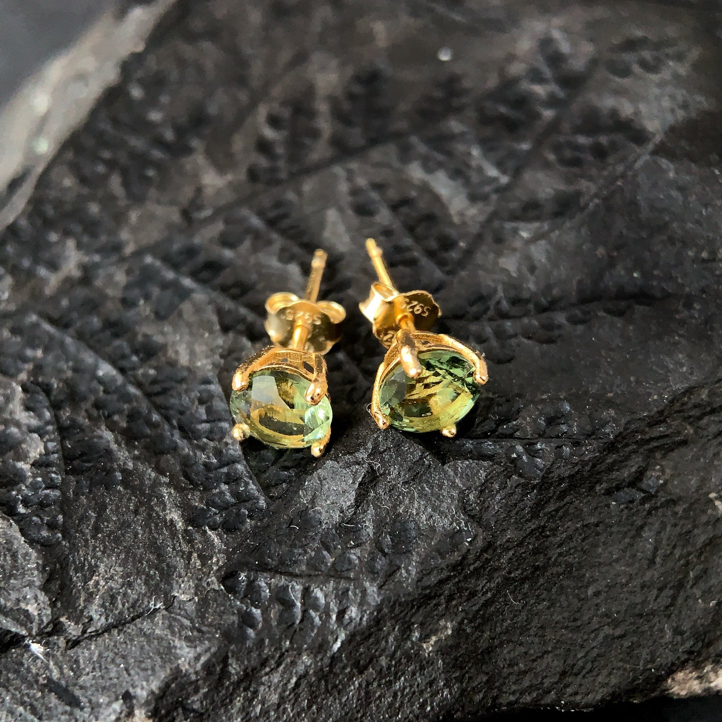 Gold plated earrings with 6mm Moldavite on a dark textured surface