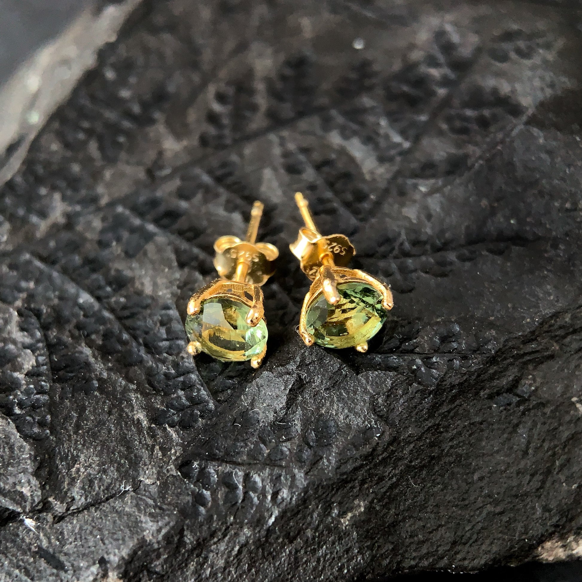 Gold plated earrings with 6mm Moldavite on a dark textured surface