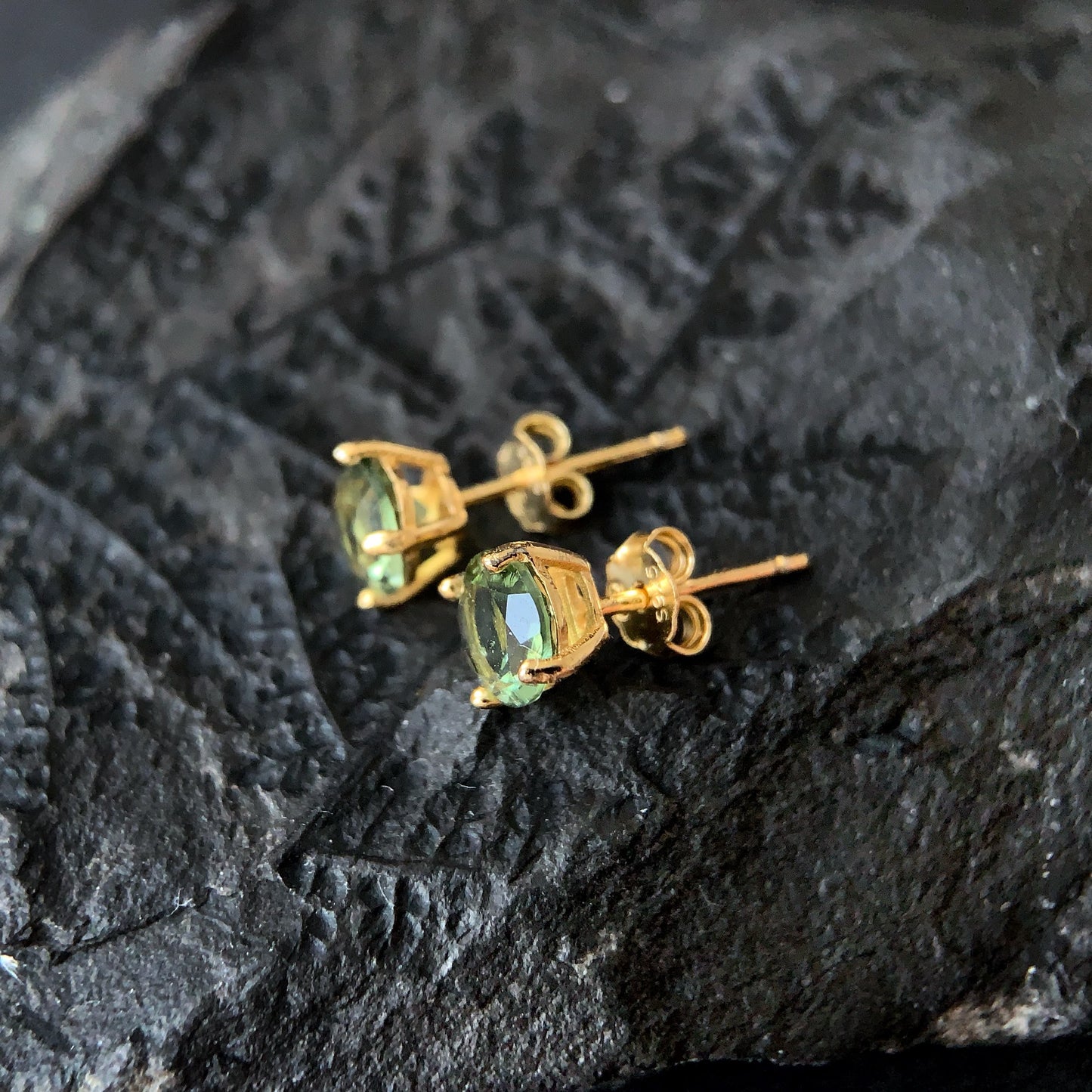 Gold plated earrings with green gemstones on a dark stone surface