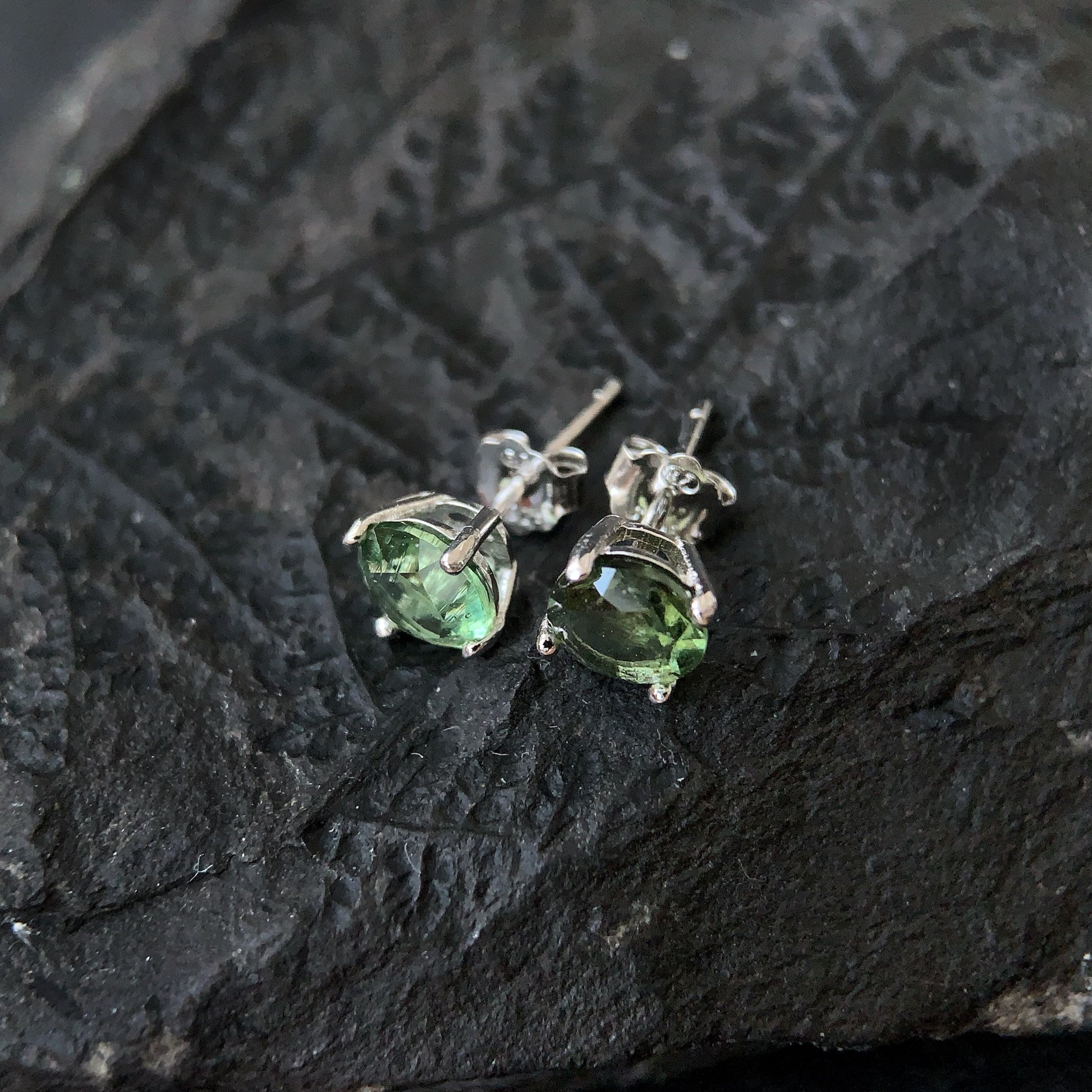 Real Moldavite earrings on a textured black stone surface