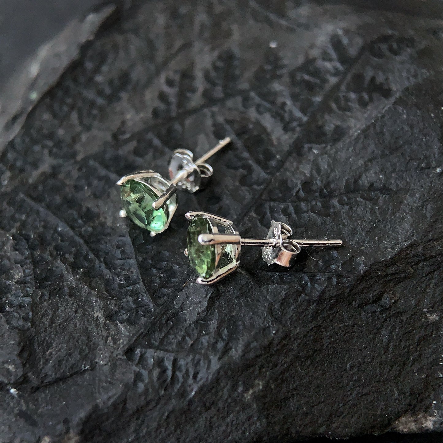 Pair of green gemstone stud earrings on a dark textured surface