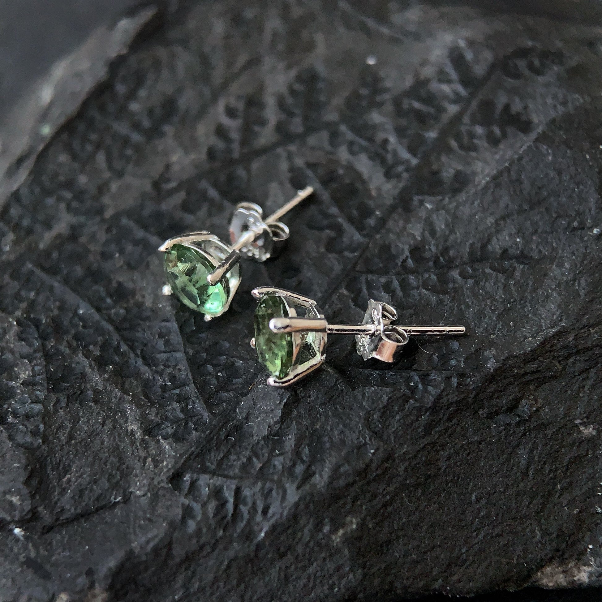 Pair of green gemstone stud earrings on a dark textured surface