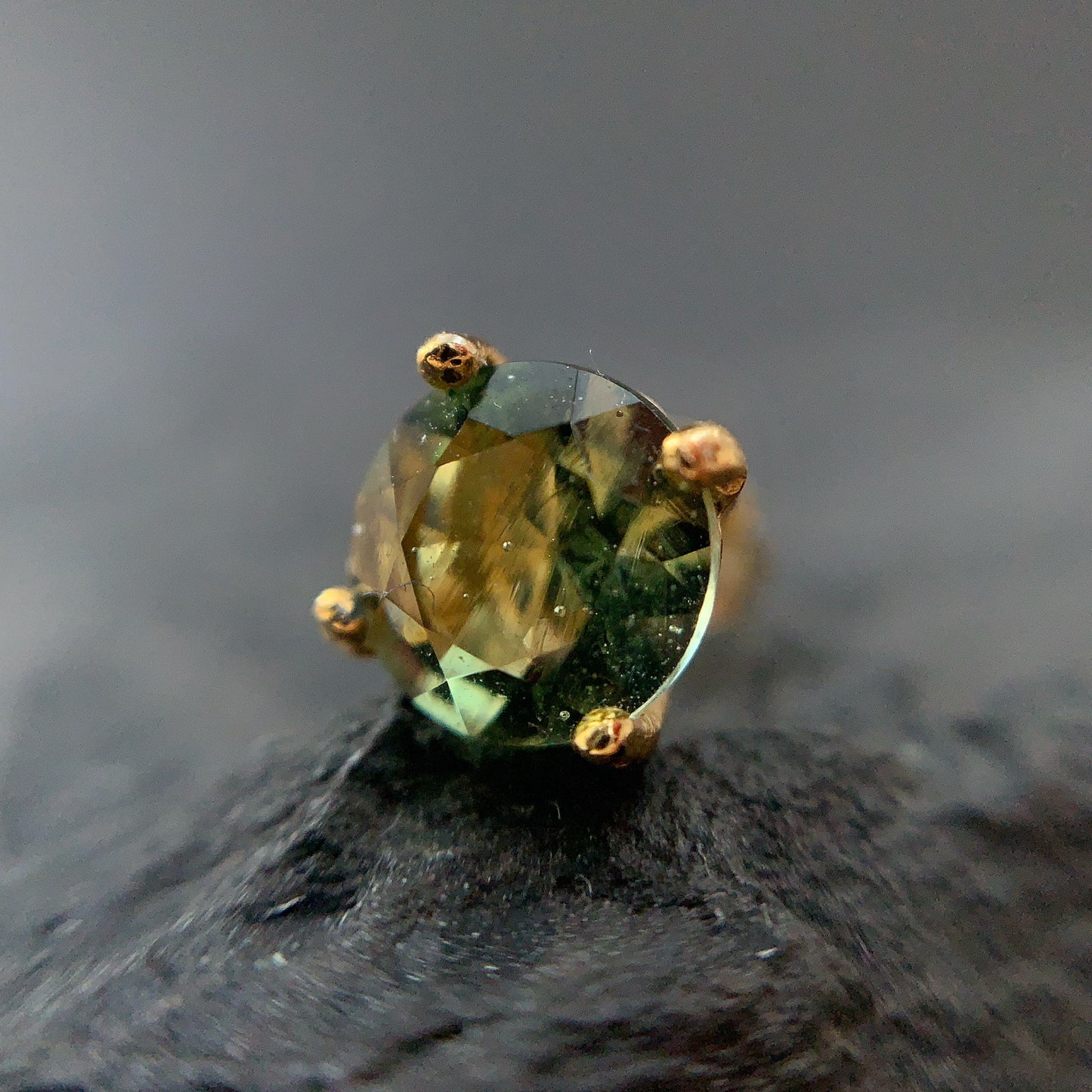 Gold plated earring with a moldavite on a dark surface