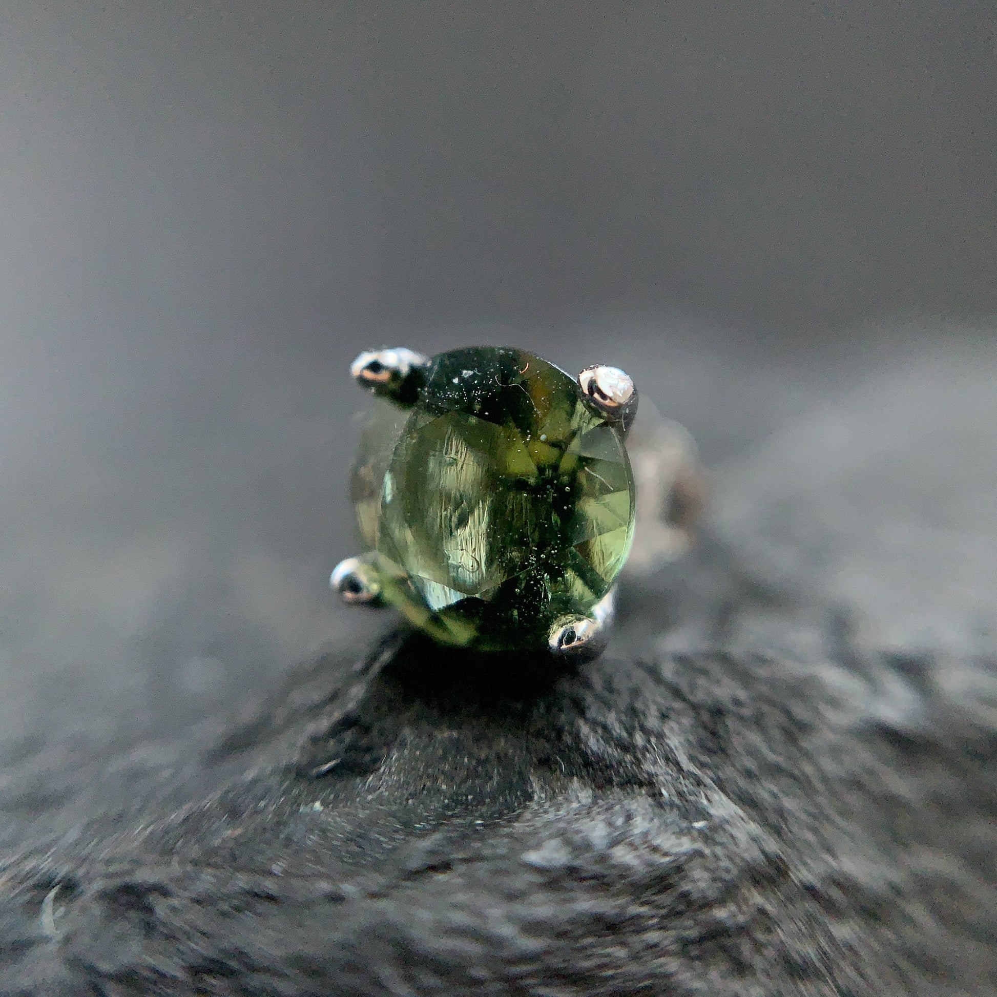 Green gemstone earring on a dark stone surface with a blurred background