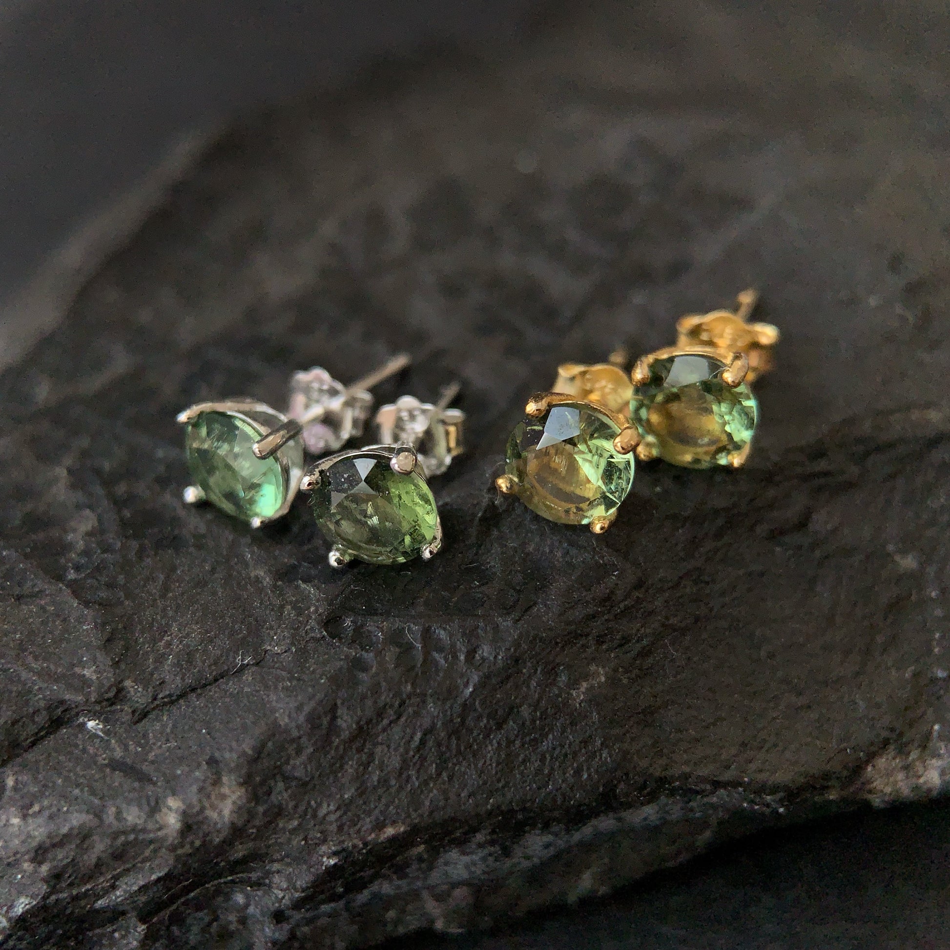 Pair of green gemstone earrings on a dark stone surface