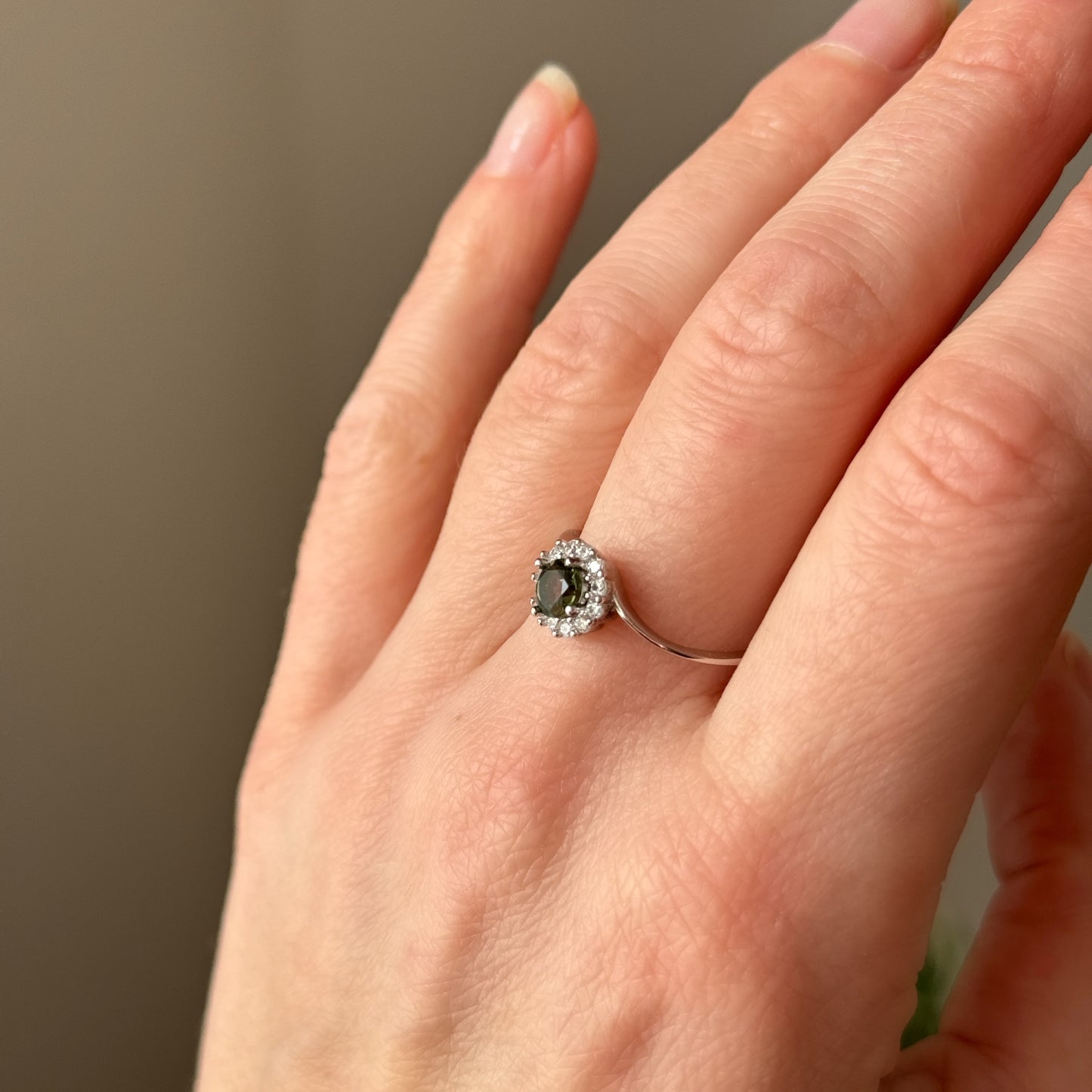 Woman hand wearing a ring with a moldavite gemstone on a neutral background